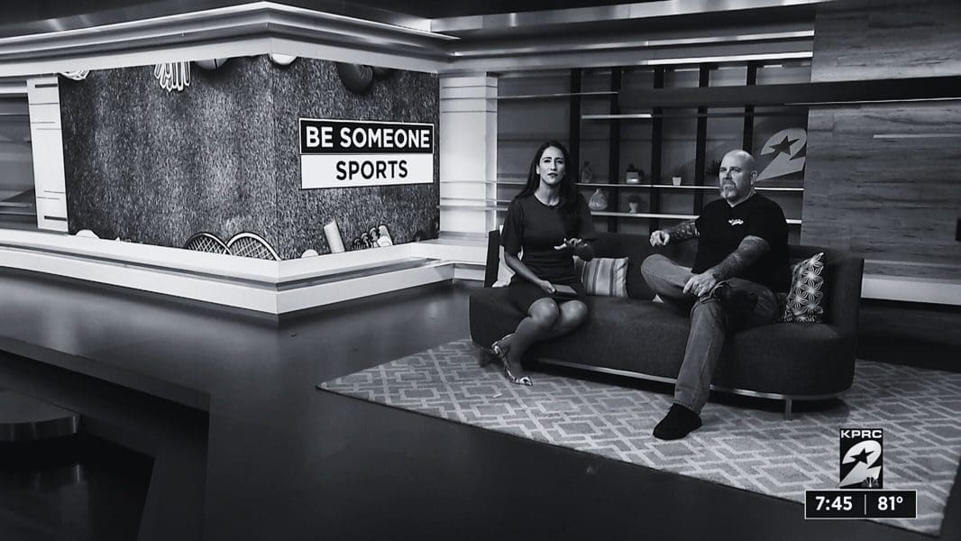 A couple sitting on the couch in front of a sign.