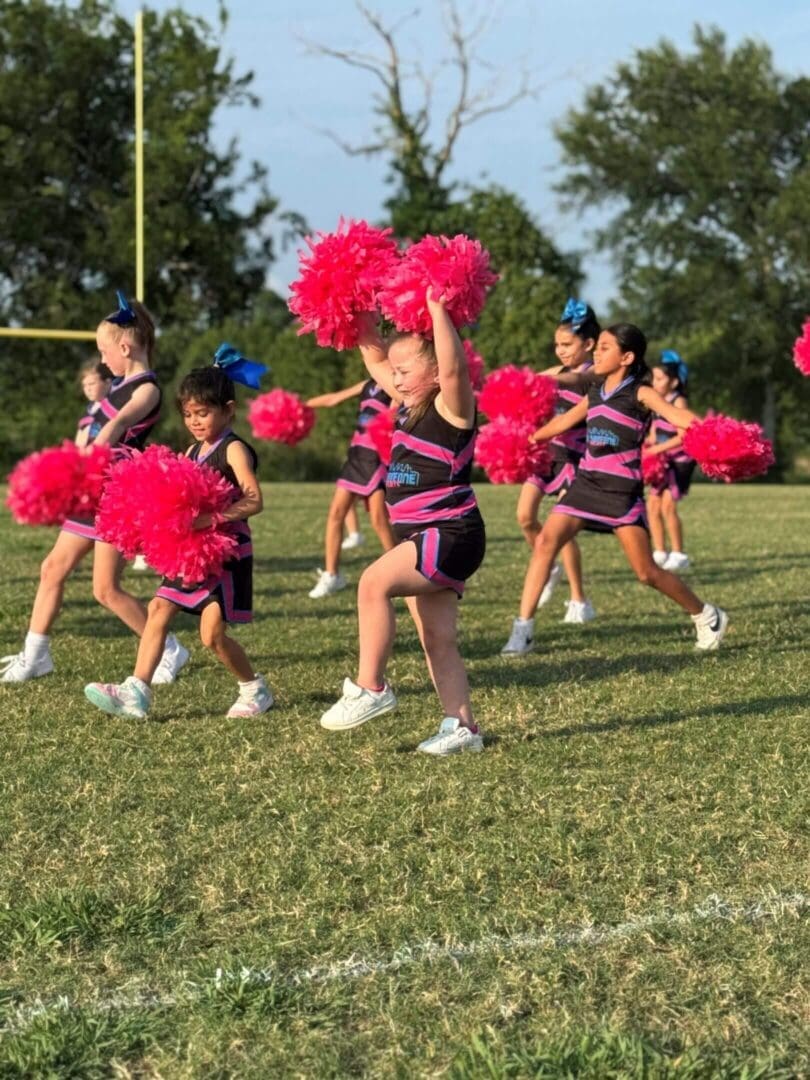 Children cheerleading with pink pom-poms outside.